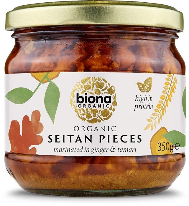 A glass jar of Biona Organic Seitan Pieces marinated in ginger and tamari. Transparent, cylindrical jar with a metal screw-top lid. The matte-finish front label shows stylized leaves and grains graphics, “high protein” text, weight “350g”, and the brand name in bold sans-serif typeface. The product sits against a plain, light background with no people or actions visible.
