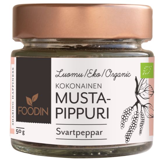 A small clear glass jar of Foodin organic whole black pepper, labeled in Finnish and Swedish, cylindrical shape with a metallic rose-gold screw-top lid. The label includes an illustration of black peppercorns and simple sans-serif typography. Single product against a neutral, plain background. No people or hands visible in the image.