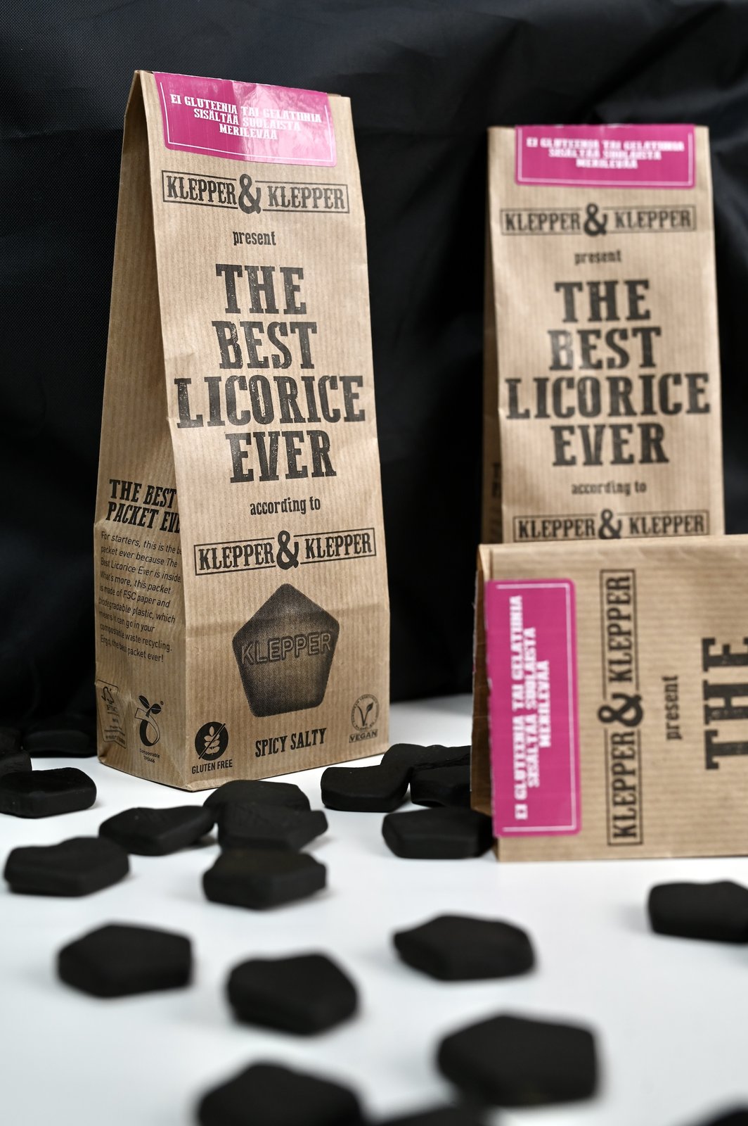Kolme Klepper & Klepper Spicy Salty -lakritsipussia mustaa taustaa vasten, etualalla salmiakkipaloja