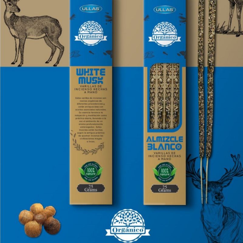 Two boxes of organic incense sticks (White Musk and Almizcle Blanco) are displayed upright on a blue and tan background, featuring deer illustrations and hazelnuts. Rectangular cardboard boxes have matte surfaces with distinct label fonts; one uses thin sans-serif, the other bold serif. Both feature prominent green and white certification seals for organic products. No people or hands visible in the shot.