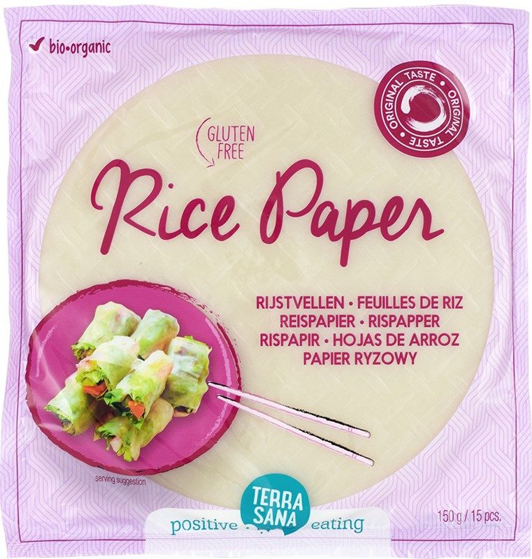 Package of TerraSana rice paper with spring rolls pictured on a pink plate. Round, clear plastic packaging with blue and white labels; matte finish. Sans-serif bold typography is used for main product name and highlighted information. The package and plate rest on a solid surface in a well-lit studio setting. Text highlights gluten-free, organic, and plant-based product info in multiple languages.