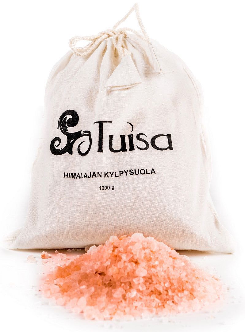 Tuisa Himalajan Kylpysuola; kangaspussi tekstillä "Tuisa Himalayan Kylpysuola 1000g" seisoo puhtaiden vaaleanpunaisten Himalajan kylpysuolakiteiden kasan takana levitettynä eteen; pussi luonnonvalkoista puuvillaa nyörillä, yksinkertaista mustaa painettua tekstiä ja mattapinta; kylpysuolakiteet epäsäännöllisiä paloja vaalean- ja keskivaaleanpunaisina; tausta valkoinen, ei ihmisiä tai tarvikkeita näkyvissä.