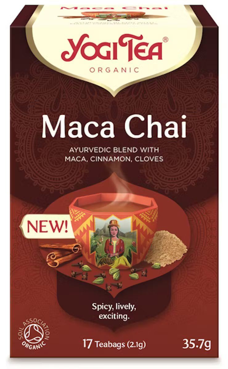 Front of a Yogi Tea Maca Chai box. Rectangular cardboard packaging with matte surface. Predominantly red design, showing a steaming cup and illustrated spices on the front. White serif and sans-serif text includes “Ayurvedic blend with maca, cinnamon, and cloves” and “Spicy, lively, exciting.” No people or hands visible. Plain background. Shot is centered and well-lit.