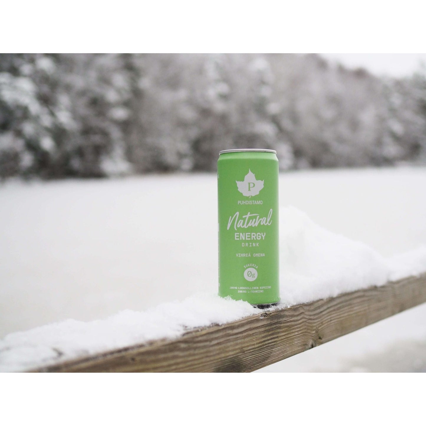 Vihreä Natural Energy Drink -tölkki lumisella puukaiteella talvimaisemassa