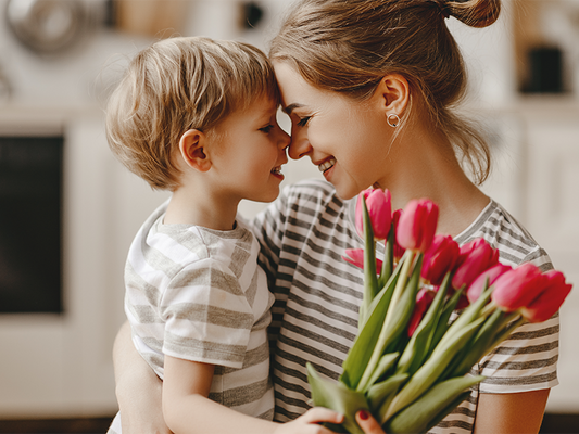 Äiti ja lapsi hymyilevät toisilleen, lapsella on kimpullinen punaisia tulppaaneja kädessään