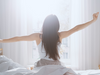 Tummahiuksinen nainen venyttelee sängyllä nukuttuaan hyvät yöunet Puhdas+ Good Night Magnesium -juomajauheen avulla