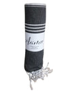 A rolled, dark gray towel with white stripes and fringed ends, labeled Aamu in script on a soft, absorbent band around the middle. The band is a solid color fabric wrap placed at the center of the towel roll. The script lettering is white and legible. The photo uses a plain background with no visible setting or people.