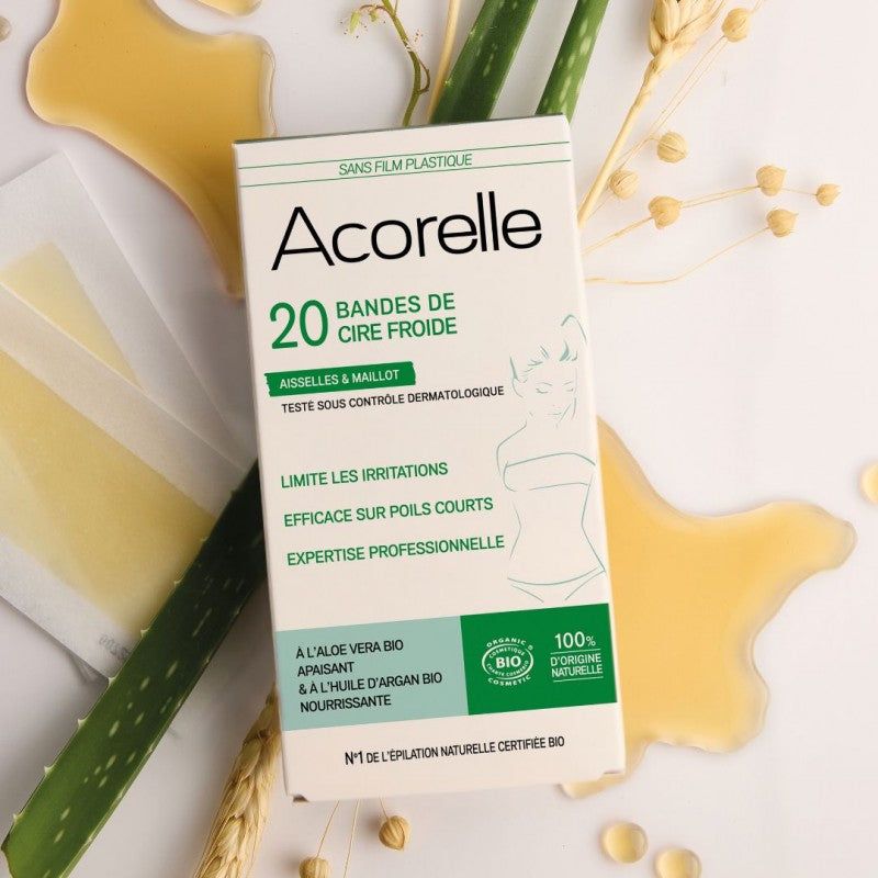 Acorelle Karvanpoistoliuskat Kainaloille ja Bikinialueelle: 20 kappaleen kylmävahaliuskapakkaus kainaloille ja bikinialueelle asetettuna valkoiselle pinnalle yhdessä aloe vera -lehtien, vehnänkorsien ja hunajamaisen vahavalumman kanssa; suorakulmainen mattavalkoinen rasia, vihreää groteskitekstiä, luomusertifikaatin merkki sekä ohut viivapiirros naisesta; ei ihmisiä tai käsiä varsinaisesti kuvassa.
