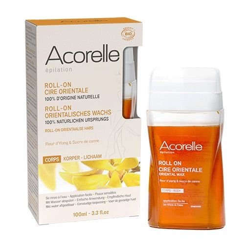 Acorelle Sokerointivaha Roll-On: pakkauslaatikko vasemmalla ja oranssi roll-on-vahasäiliö oikealla, molemmissa tuotetietoja usealla kielellä ja mainintoja luonnollisista ainesosista tehokkaaseen karvanpoistoon; suorakulmainen mattapintainen laatikko valkoisin ja keltaisin korostuksin, pystyasento, musta groteskikirjasin; vahasäiliö on läpikuultavaa oranssia muovia, sylinterimäinen, valkoinen korkki ja rullapää; tausta on valkoinen, ei ihmisiä tai toimintaa näkyvissä.