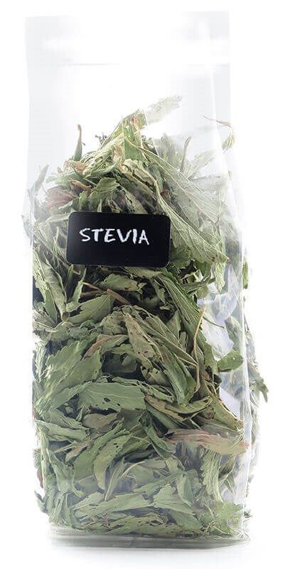 Aduki Luomu Stevian lehti; kirkas muovipussi täynnä kuivattuja steviankukkalehtiä, etiketissä lukee Stevia Leaf mustassa tarrassa; pussi suorakulmainen rypistyneellä pinnalla ja kuumasaumatulla yläreunalla; sisältö vaaleanvihreää ja näkyy läpinäkyvän pakkauksen läpi; musta matta etiketti lihavoidulla valkoisella groteskikirjasimella; kuva otettu valkoista taustaa vasten ilman ihmisiä tai esineitä.