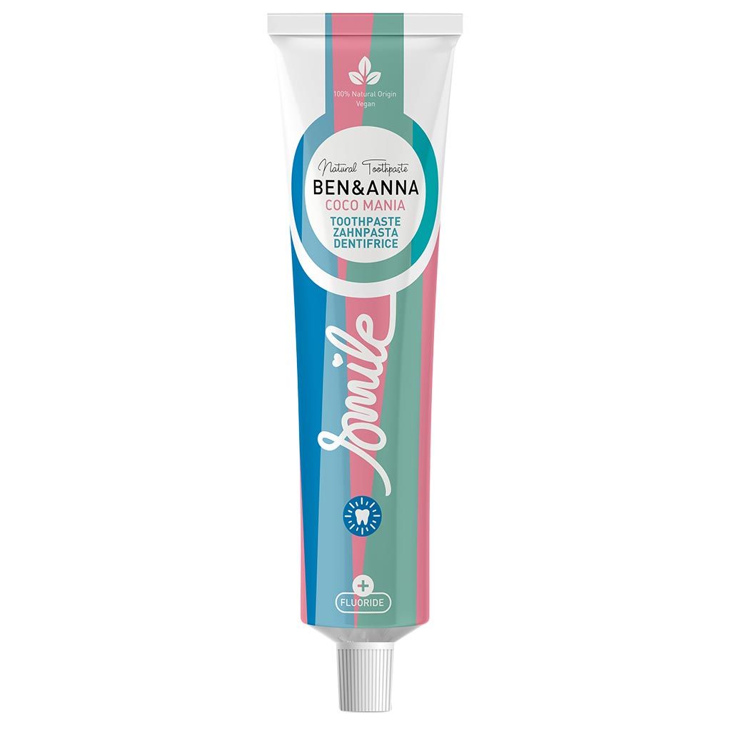 A tube of Ben & Anna toothpaste labeled Coco Mania features green, pink, and blue stripes with the word “Smile” in white. The packaging highlights fluoride content and 100% natural origin ingredients. The tube is cylindrical with a matte finish and vertical label text. Typeface is modern sans-serif, main colors are visible on a white background. No people or props are present; product shot is centered.