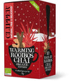 Clipper Luomu Rooibos Chai; punainen laatikko Clipper Warming Rooibos Chai -luomuteelle, kuvituksena musta teekuppi kanelitankojen, tähtianiksen ja punaisten lehtien kera; suorakulmainen pakkaus mattapinnalla; valkoinen sans-serif-teksti tunnistaa luomutuotteen; taustalla tyylitellyn lumen ja talojen kuvitusta; ei ihmisiä tai käsiä kuvassa.