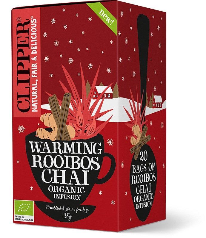 Clipper Luomu Rooibos Chai; punainen laatikko Clipper Warming Rooibos Chai -luomuteelle, kuvituksena musta teekuppi kanelitankojen, tähtianiksen ja punaisten lehtien kera; suorakulmainen pakkaus mattapinnalla; valkoinen sans-serif-teksti tunnistaa luomutuotteen; taustalla tyylitellyn lumen ja talojen kuvitusta; ei ihmisiä tai käsiä kuvassa.