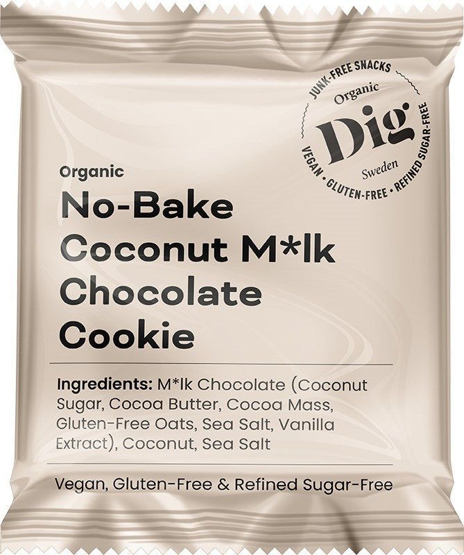Dig Luomu Kookossuklaakeksi; beige, mattapintainen suorakulmainen pussi, merkitty ”Dig Organic No-Bake Coconut M*lk Chocolate Cookie”; etupuolella lihavaa groteski- ja kaunokirjoitusfonttia, jossa vegaani-, gluteenitonta ja puhdistetusta sokerista vapaata koostumusta koskevat väitteet ja luomu-ainesosaluettelo; ei ihmisiä tai käsiä näkyvissä; tausta vaalea, koko pussi näkyvissä kuvassa.