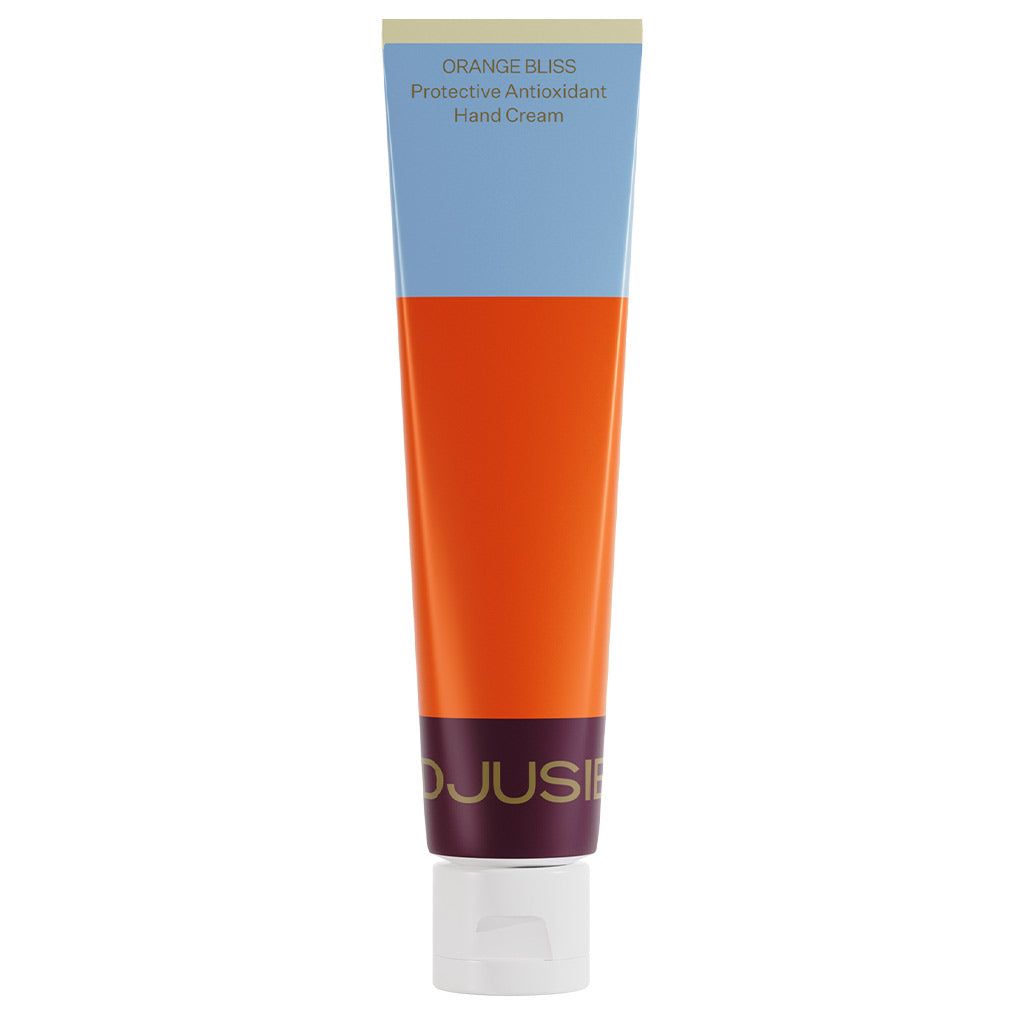 A tube of hand cream labeled ORANGE BLISS Protective Antioxidant Hand Cream stands upright with a white cap. The packaging displays blocks of vibrant blue, orange, and maroon with a matte finish. The tube is cylindrical and made of flexible material. The label uses bold, sans-serif typography in various sizes. There are no hands or people visible. Plain background.