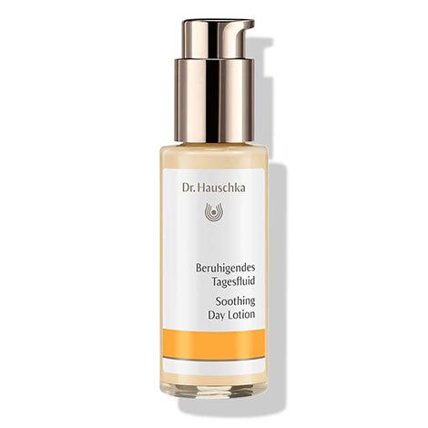 A bottle of Dr. Hauschka Soothing Day Lotion with a gold pump and white label, featuring calming text in German and English and an orange band near the bottom. The bottle is cylindrical with a matte finish. The label uses sans-serif black lettering; “Soothing Day Lotion” is the main text visible. The background is plain white, product centered, no people or hands in the image.