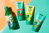 Four green ESI Aloe Vera gel tubes, made of glossy plastic and featuring a tapered shape with flip-top caps, are arranged diagonally on a background split into yellow and teal halves. Sunlight produces defined shadows behind the products. Labels use clean sans-serif fonts and mention pure aloe vera or added vitamins as ingredients. No people or hands are visible in the shot.