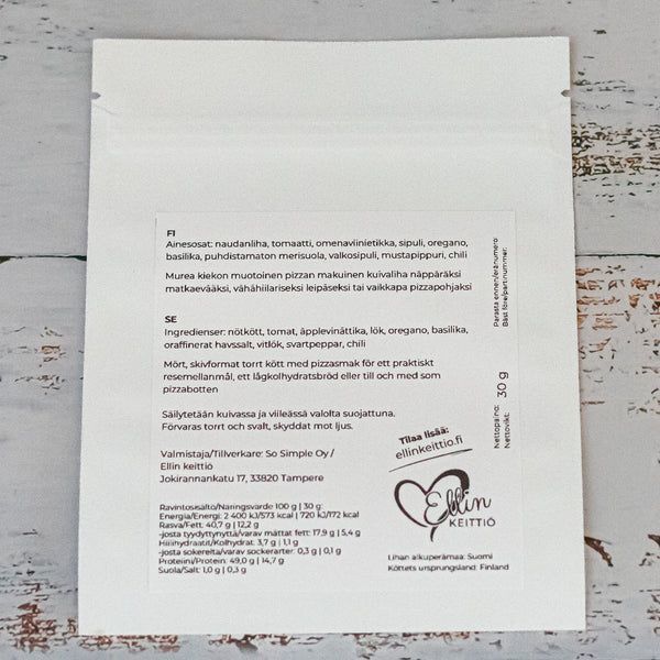 Ellin Lihakiekko Pizzamausteinen; valkoinen elintarvikepussi valmistusohjeineen ja ainesosineen suomeksi ja ruotsiksi rustiikkisella, valkoiseksi maalatulla puupinnalla; mattapintainen pakkaus suorakaiteen muotoinen, painetussa etiketissä näkyvää tikkukirjasinta, Ellin Keittiö -logo, sydänsymboli ja yrityksen osoite; ei ihmisiä tai käsiä näkyvissä; keskikokoinen kuva neutraalissa valaistuksessa.