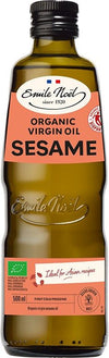 A 500ml bottle of Emile Noël organic virgin sesame oil with a green cap, brown glass, and a beige and orange label showing fair trade and organic certifications. Cylindrical bottle; cap is smooth, plastic. Label uses serif fonts for brand name and sans-serif for other information. Key certifications are in icon form near the label bottom. Plain white background with no props or people. Studio product shot at eye level.