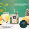 Foodin Green Superfood Tropical Energy; purkki pöydällä vihreää mehulasia sekä hedelmien ja tuoreiden raaka-aineiden ympäröimänä; muovipurkki lieriön muotoisena mattapintaisella etiketillä, suomenkielinen groteskiteksti tiivistää keskeiset kasviperäiset ainesosat; hyvin valaistu tausta pehmeästi sumennettuna, ei ihmisiä tai käsiä.