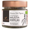 A small clear glass jar of Foodin organic whole black pepper, labeled in Finnish and Swedish, cylindrical shape with a metallic rose-gold screw-top lid. The label includes an illustration of black peppercorns and simple sans-serif typography. Single product against a neutral, plain background. No people or hands visible in the image.