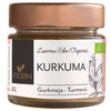 A small glass jar of Foodin organic turmeric powder is shown with a cylindrical clear container and a metallic copper-colored screw-on lid. The label, printed in Finnish, Swedish, and English, features minimalist botanical illustrations and sans-serif typography. Product name and descriptions are legible on the front. The background is plain white with no people or hands visible.