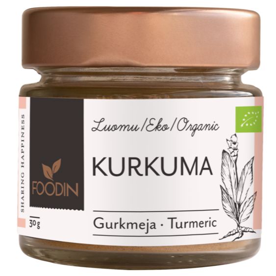 A small glass jar of Foodin organic turmeric powder is shown with a cylindrical clear container and a metallic copper-colored screw-on lid. The label, printed in Finnish, Swedish, and English, features minimalist botanical illustrations and sans-serif typography. Product name and descriptions are legible on the front. The background is plain white with no people or hands visible.
