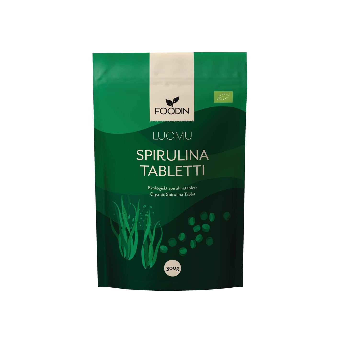 A green package of Foodin organic spirulina tablets, labeled Luomu Spirulina Tabletti. The packaging is rectangular with a matte finish and has stylized seaweed graphics and bright green accent details. A round label at the bottom displays “300g.” Sans-serif typography is used. The product stands alone against a neutral background in a studio shot.