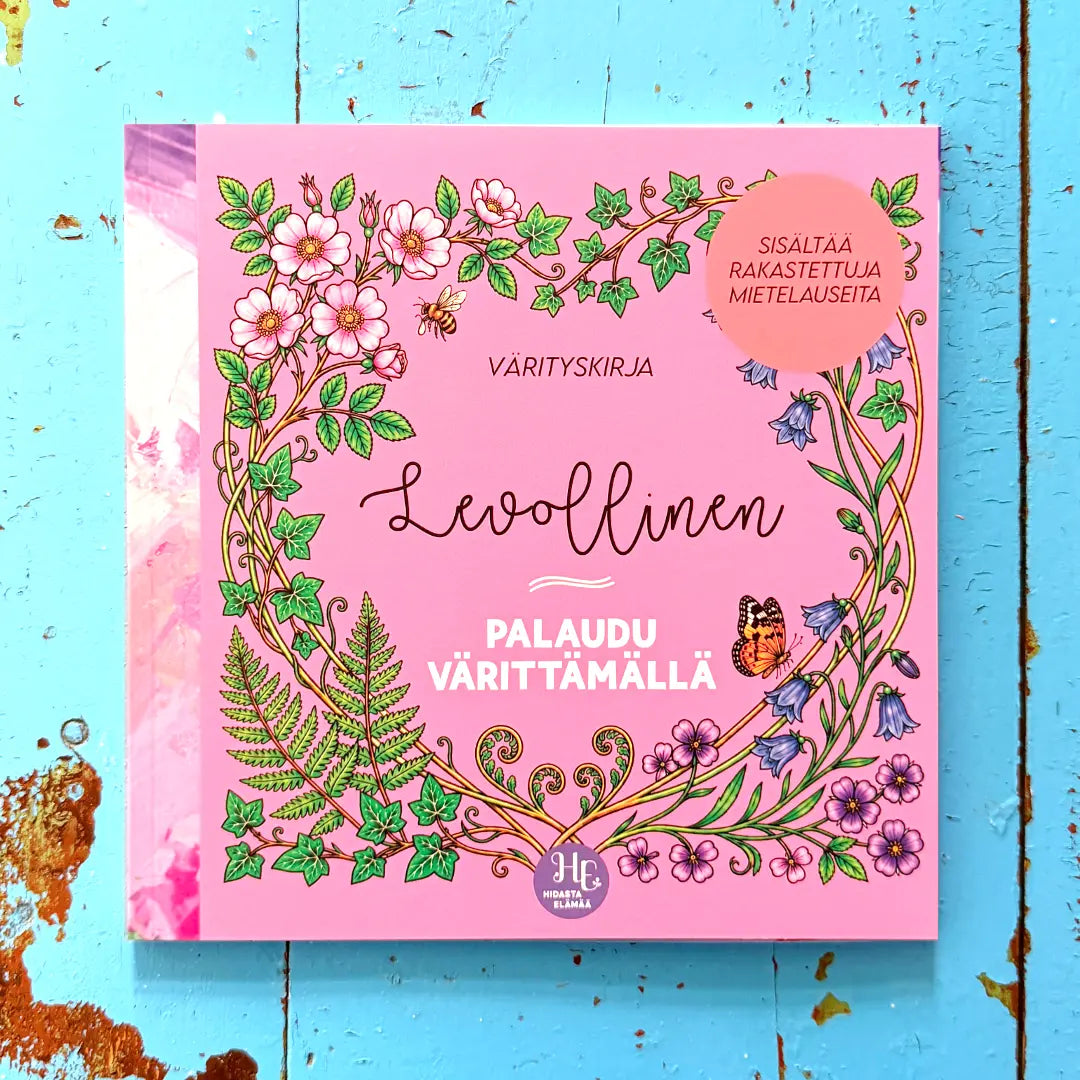 Levollinen-värityskirjan kansi valokuvattuna turkoosilla puupöydällä