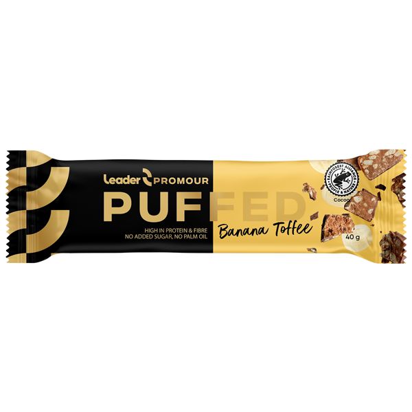 A yellow and black wrapper for Leader Promour Puffed Banana Toffee bar, featuring images of the bar and its ingredients. Matte packaging with both serif and sans-serif text styles. Front of package displays product name, flavor, and icons or text for high protein, fiber, no added sugar, no palm oil. Bar shape is rectangular. Neutral studio background with no hands or people visible.
