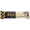 A Leader Promour Puffed Cookies & Cream protein bar in sleek black, gold, and white packaging, featuring cookie and cream pieces, with text highlighting high protein and no added sugar content. Packaging is rectangular with a glossy finish. Typography is bold and sans-serif in white and gold. Product lies on a plain surface with no background details visible. No people or hands present in the image.
