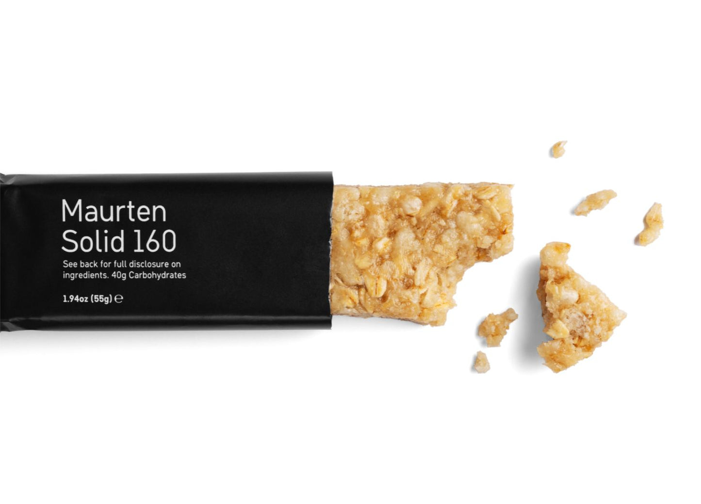 A partially unwrapped Maurten Solid 160 energy bar with a bite taken out and some crumbs scattered on a white background, showcasing its convenient, high-energy design. Rectangular bar with rough surface, dark brown color. Matte finish on both bar and packaging. Packaging is black with bold white sans-serif text reading “Maurten Solid 160.” No people or hands visible; close-up product shot.