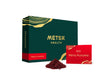 A green rectangular box with gold trim and a matte finish displays METSA HEALTH and Mänty Puolukka in clear, sans-serif type on a red label. Next to the box is a single-use red sachet, also rectangular, and a small mound of finely ground dark red powder. All items are set against a plain background with no people or actions visible.