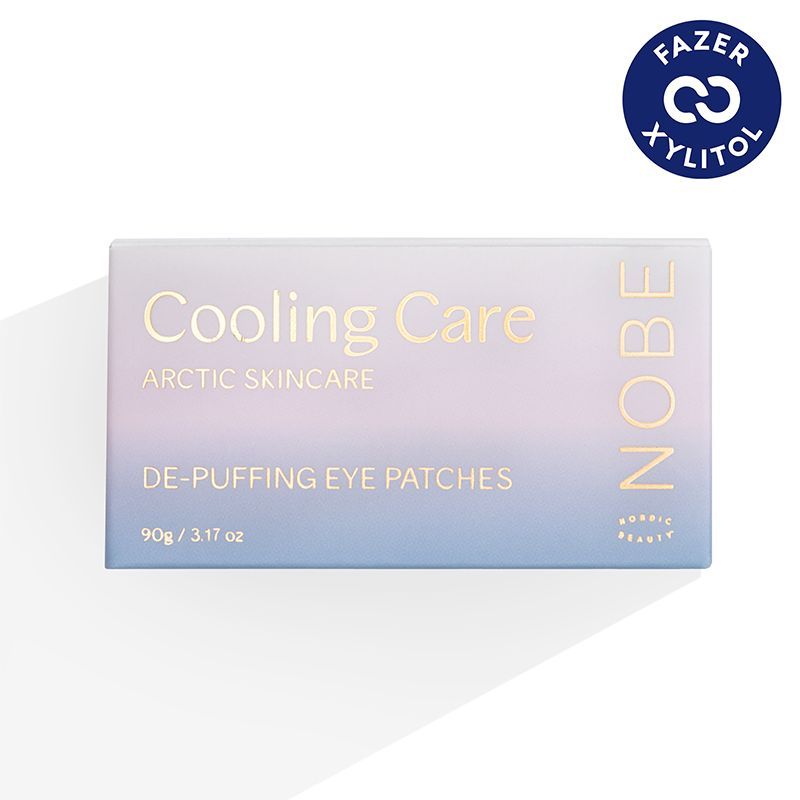 NOBE Cooling Care De-Puffing Eye Patches; suorakulmainen laatikko tekstillä "Cooling Care Arctic Skincare De-Puffing Eye Patches" ja NOBE oikealla puolella; kulmassa sininen pyöreä merkki tekstillä "FAZER XYLITOL"; tausta valkoinen pehmeine varjoineen; laatikko suorareunainen mattapinnalla; sans-serif-tekstiä eri kokoina; ei ihmisiä tai käsiä; studiokuva suoraan edestä.