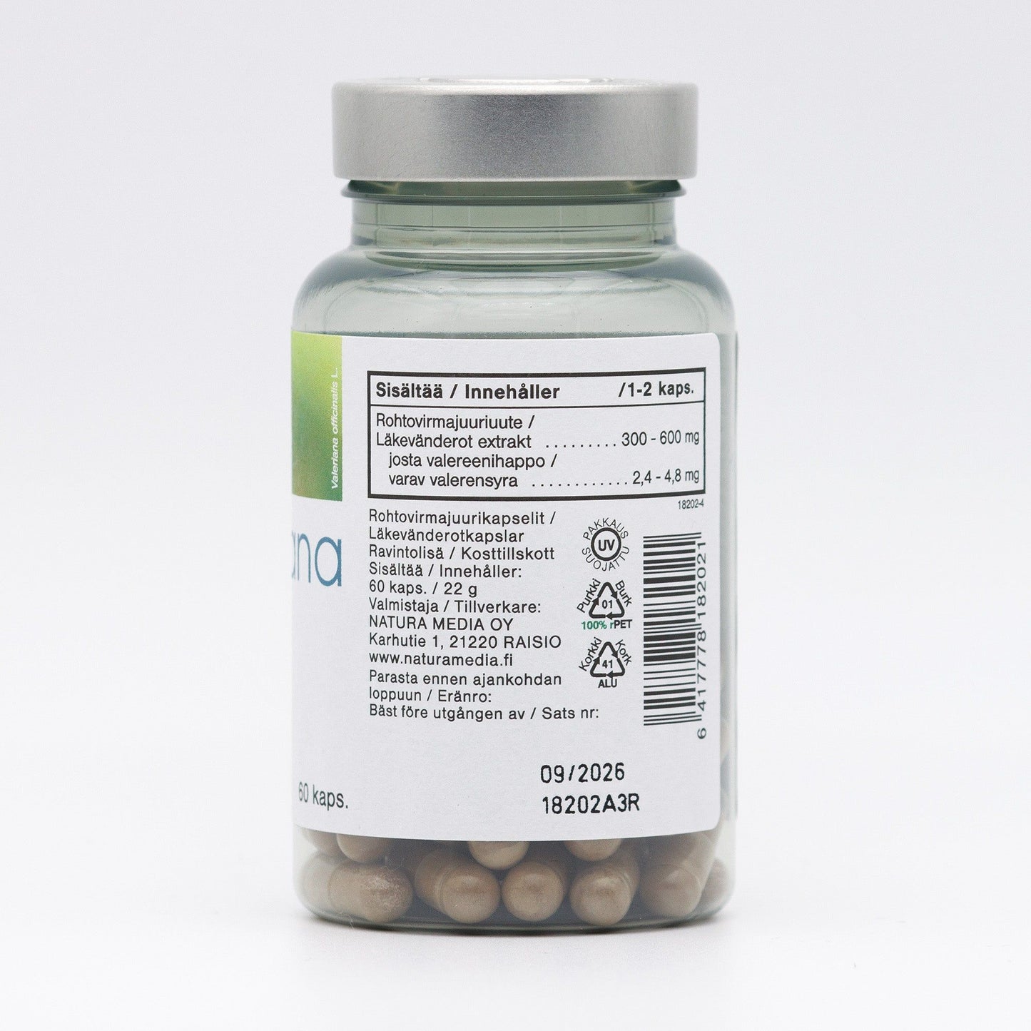A clear bottle with a silver lid contains round brown capsules. The bottle is cylindrical with smooth surfaces and a glossy finish. The label, mostly white, features sans-serif text in black and blue with nutrition data, ingredients in both Finnish and English, a barcode, manufacturing info, and 09/2026 as the expiration date. Nutritional information occupies a central area of the label. The background is plain white.