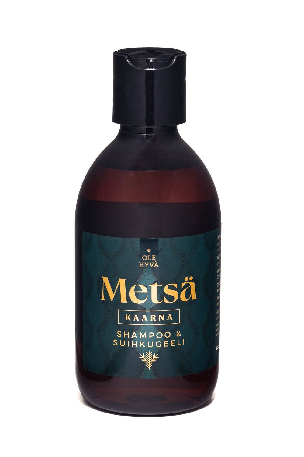 A dark brown bottle with a black cap labeled Ole Hyvä Metsä Kaarna Shampoo & Suihkugeli features a teal and gold label. The bottle is cylindrical with a matte finish. The label uses bold sans-serif typography in white and gold on a teal background with abstract pattern accents. The product is photographed upright against an even, neutral background with no people or hands visible.