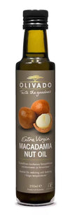 A bottle of Olivado Extra Virgin Macadamia Nut Oil with a brown, glossy label and images of whole and cracked macadamia nuts. The bottle is cylindrical, dark glass, 250ml size. Legible text on the label includes product name and origin details. Background is plain and neutral. No people or hands are visible in the image.