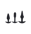 Three black silicone anal plugs of varying shapes and sizes are displayed upright against a plain white background. The surface is matte without visible seams or text. Each plug has a flared base, with differences in contour and length. There is no packaging, typography, or additional objects present. The shot is a front-facing studio product photo with even lighting; no people or hands are shown.
