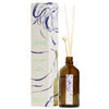 Brown glass reed diffuser bottle with wooden sticks beside a white rectangular box. The box has a matte surface, blue abstract art on the front, and green uppercase SEES lettering. No visible branding on the bottle or sticks. Set against a plain background with no people present. Shot is taken from the front at eye level.