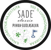 Circular product label for SADE classic PIHKA-SUOLASALVA, featuring green flowers, a Finnish flag symbol, and Finnish text indicating it is 100% natural cosmetics. Label is printed on a matte surface with clear sans-serif typography. Shot is a close-up; only the product label is visible against a neutral background. No people or hands present.