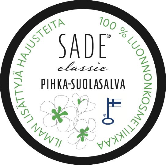 Circular product label for SADE classic PIHKA-SUOLASALVA, featuring green flowers, a Finnish flag symbol, and Finnish text indicating it is 100% natural cosmetics. Label is printed on a matte surface with clear sans-serif typography. Shot is a close-up; only the product label is visible against a neutral background. No people or hands present.