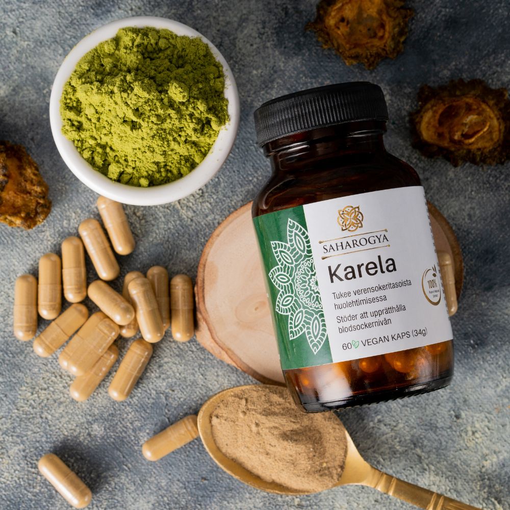 A bottle of Saharogya Karela capsules with a white plastic body and green cap features green and black printed label text. The bottle is placed on a matte, textured surface alongside a small bowl containing fine green powder, loose tan capsules, several sliced pieces of fresh karela (bitter melon), and a metal spoon holding more karela powder. No people or hands are present. A bottle of Saharogya Karela capsules is surrounded by green powder in a bowl, tan capsules, sliced karela pieces, and karela powder