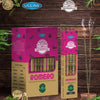 Boxes and sticks of Ullas Orgánico Romero incense are displayed on a wooden surface, with two incense sticks burning and light smoke rising. The packaging is rectangular in shape, colored pink and beige with a matte finish. Botanical illustrations appear on the boxes. Sans-serif text lists organic ingredients and product information in clear lettering. No people or hands present. Medium shot captures all items on the wood background.
