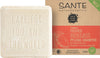 Sante Family Solid Moisturizing Care Palashampoo; kiinteä shampoopala kohokuvioidulla tekstillä "Care for you and the world" lepää pahvilaatikon vieressä merkinnällä Sante Naturkosmetik Festes Feuchtigkeitspflege-Shampoo, vegaani- ja sertifioitu luonnonkosmetiikkakuvakkein; shampoo on vaaleanvärinen mattapinnalla pyöristetyin reunoin; laatikossa lohkomaista painettua tekstiä, kuvitettu design ja symboleja etuosassa; tausta yksivärinen, ei ihmisiä tai käsiä näkyvissä; kuva on suoraviivainen tuotekuva.
