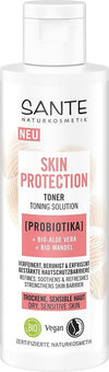 Sante Skin Protection Kasvovesi; valkoinen sylinterinmuotoinen pullo merkitty Sante Naturkosmetik Skin Protection Toner seisoo pystyssä; pinta mattapintainen, teksti painettu selkeällä groteskikirjasimella; etiketissä vegaani- ja luomusertifiointimerkinnät; pullossa mainitaan probiootti, luomu-aaloe vera ja luomu-manteli kuivalle tai herkälle iholle; kuvan tausta yksivärinen.