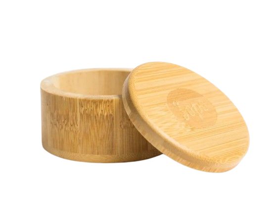 Round bamboo container with a matching lid, shown slightly open. The surface is smooth and light-colored, displaying visible natural wood grain. The lid has a circular logo etched on top in a subtle manner. No additional text is present. Set against a plain light gray background with even lighting; no people or hands appear in the image.