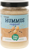 Terrasana Luomu Hummus; lasipurkki luomuhummusta mustalla kannella; etiketti on sininen ja beige mattapinnalla, kääritty sylinterinmuotoisen kirkkaan lasipurkin ympärille; etuosassa kuvituksia kikherneistä ja seesaminsiemenistä; groteskitekstiä tuotetiedoissa, näkyvissä maininta "positive eating"; tausta on yksivärinen valkoinen, ei ihmisiä tai muita esineitä näkyvissä.