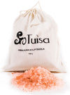 Tuisa Himalajan Kylpysuola; kangaspussi tekstillä "Tuisa Himalayan Kylpysuola 1000g" seisoo puhtaiden vaaleanpunaisten Himalajan kylpysuolakiteiden kasan takana levitettynä eteen; pussi luonnonvalkoista puuvillaa nyörillä, yksinkertaista mustaa painettua tekstiä ja mattapinta; kylpysuolakiteet epäsäännöllisiä paloja vaalean- ja keskivaaleanpunaisina; tausta valkoinen, ei ihmisiä tai tarvikkeita näkyvissä.