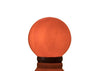A round, glowing Himalayan salt lamp sits on a small dark wooden base against a plain white background. The lamp is orange-pink with a matte, uneven crystalline surface. The base is smooth and circular. There is no visible wiring or label text in the image. The product is unboxed and photographed alone with no people or hands present.