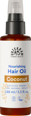 A bottle of Urtekram Nordic Beauty Nourishing Hair Oil, Coconut variety, 100 ml. The bottle is cylindrical with a pump dispenser and transparent body, showing light yellow oil inside. Label is matte, beige with dark text in sans-serif font. Legible label notes certified organic, vegan, 100% natural origin ingredients, coconut oil. No people or hands visible; plain white background; centered product shot.